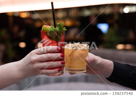 Close-up of two people clinking cocktails in a toast at a bar Close-up of two people clinking cocktails in a toast at a bar 139237540
