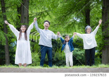 A three-generation family walking hand in hand in a park lush with new greenery; a happy family life with smiles looking directly at the camera; a full-body cheer. 139237633