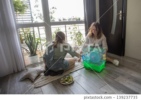 Two girls share snacks and play with a pet on a rug inside a bright room  139237735