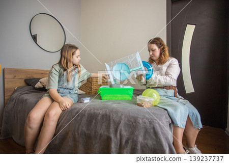 Mom and girl sit on a bed in a small room with pet. Mom and girl sit on a bed in a small room with pet. 139237737