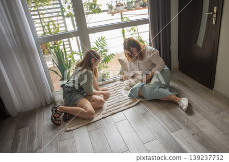 girl and women relax on a rug in a modern indoor space. They share snacks while sitting 139237752