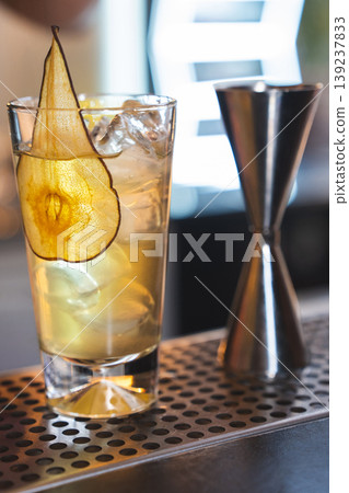 Iced cocktail with pear garnish next to a metal jigger 139237833