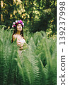 Romantic young woman in flower wreath posing among green fern leaves in summer forest 139237998