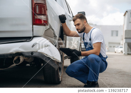 Assesses damage. Mechanic is sitting by the damaged pickup truck outdoors Assesses damage. Mechanic is sitting by the damaged pickup truck outdoors 139238717