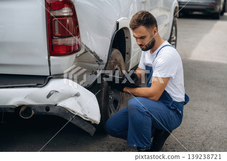 Assesses damage. Mechanic is sitting by the damaged pickup truck outdoors Assesses damage. Mechanic is sitting by the damaged pickup truck outdoors 139238721