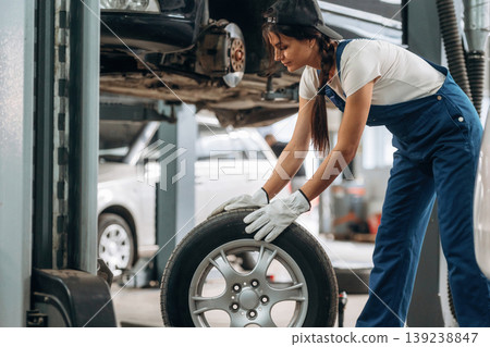 Rolling the wheel. Woman mechanic is with tire in the modern car workshop 139238847