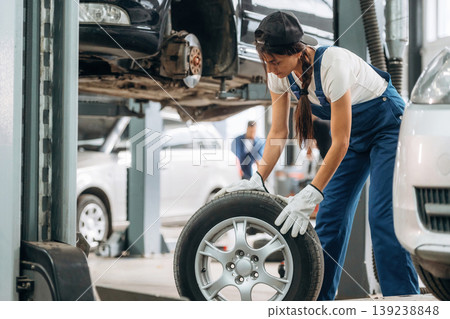Rolling the wheel. Woman mechanic is with tire in the modern car workshop 139238848