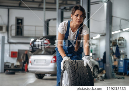 Walking and moving brand new wheel. Woman mechanic is with tire in the modern car workshop Walking and moving brand new wheel. Woman mechanic is with tire in the modern car workshop 139238883