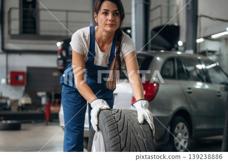 Walking and moving brand new wheel. Woman mechanic is with tire in the modern car workshop Walking and moving brand new wheel. Woman mechanic is with tire in the modern car workshop 139238886