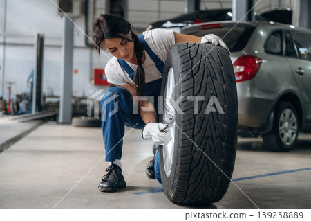 Seasonal replacement conception. Woman mechanic is with tire in the modern car workshop Seasonal replacement conception. Woman mechanic is with tire in the modern car workshop 139238889