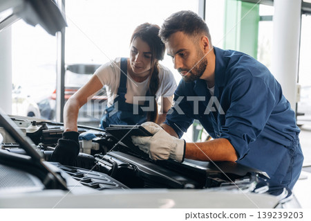 Checking electronics, hood is opened. Auto repair shop employees are working together. Man and woman 139239203