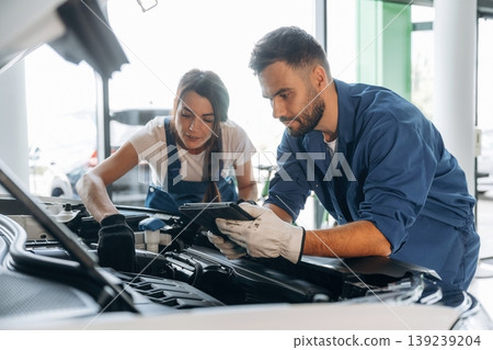 Checking electronics, hood is opened. Auto repair shop employees are working together. Man and woman 139239204