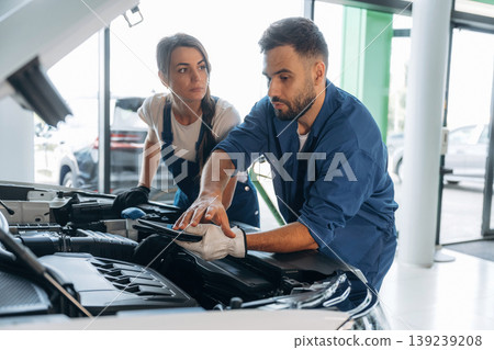 Hood is opened, checking the state of car. Auto repair shop employees are working together. Man and woman Hood is opened, checking the state of car. Auto repair shop employees are working together. Man and woman 139239208