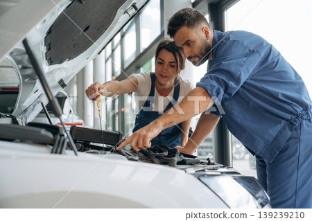 Hood is opened, checking the state of car. Auto repair shop employees are working together. Man and woman Hood is opened, checking the state of car. Auto repair shop employees are working together. Man and woman 139239210