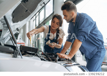 Hood is opened, checking the state of car. Auto repair shop employees are working together. Man and woman 139239212
