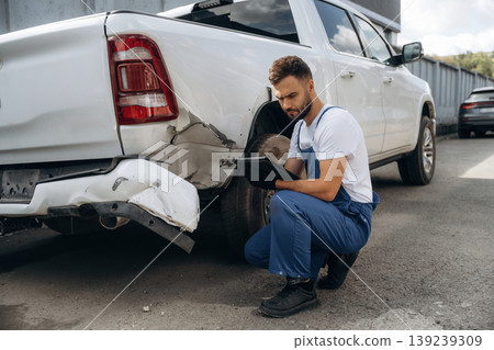 Mechanic is sitting by the damaged pickup truck outdoors Mechanic is sitting by the damaged pickup truck outdoors 139239309