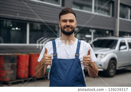 Handsome male mechanic in uniform is standing against car service station 139239317