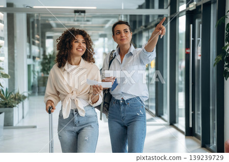 Tourists with suitcase. Two women are indoors in the modern hall of building at daytime 139239729