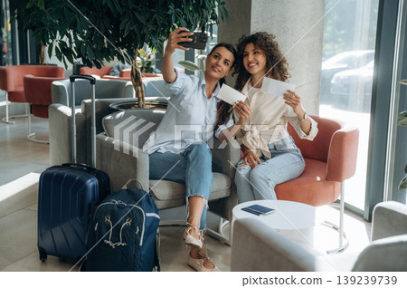 Doing selfie, tourists. Two women are indoors in the modern hall of building at daytime 139239739