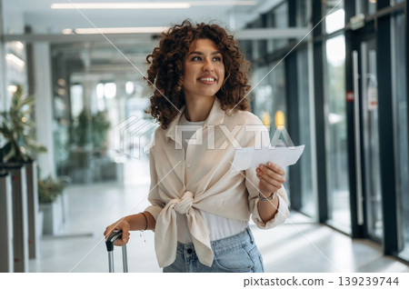 Paper document is in hand, pass, ticket. Beautiful woman is in airport hall with suitcase Paper document is in hand, pass, ticket. Beautiful woman is in airport hall with suitcase 139239744