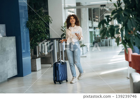 Paper document is in hand, pass, ticket. Beautiful woman is in airport hall with suitcase Paper document is in hand, pass, ticket. Beautiful woman is in airport hall with suitcase 139239746