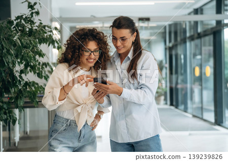 Business partners are together. Two women are indoors in the modern hall of building at daytime Business partners are together. Two women are indoors in the modern hall of building at daytime 139239826
