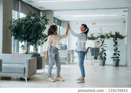 High five hands gesture. Two women are indoors in the modern hall of building at daytime 139239842
