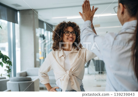 High five hands gesture. Two women are indoors in the modern hall of building at daytime High five hands gesture. Two women are indoors in the modern hall of building at daytime 139239843
