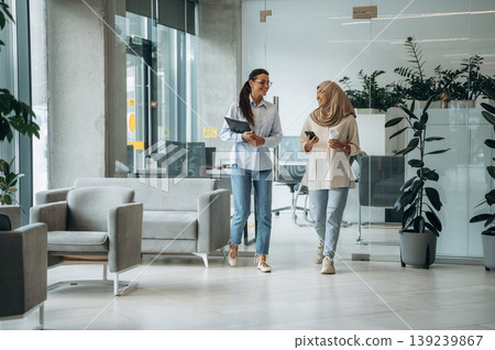 Muslim clothing. Two women are indoors in the modern hall of building at daytime Muslim clothing. Two women are indoors in the modern hall of building at daytime 139239867
