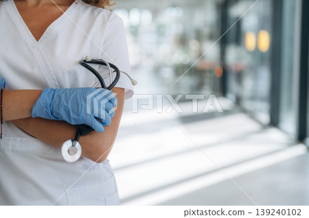 Stethoscope is in hands. Woman doctor is standing indoors in the clinic 139240102