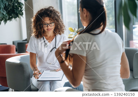 Consultation with doctor. Two women are indoors in the modern hall of building at daytime Consultation with doctor. Two women are indoors in the modern hall of building at daytime 139240150