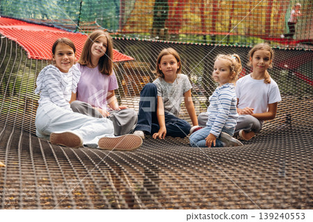 In casual clothes, relaxed, sitting. Kids are playing on the children's amusement ropes course In casual clothes, relaxed, sitting. Kids are playing on the children's amusement ropes course 139240553
