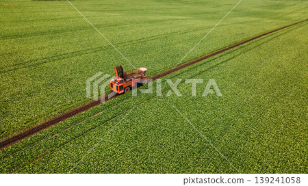 Work in progress. Aerial view of beet harvester on the green agricultural field Work in progress. Aerial view of beet harvester on the green agricultural field 139241058