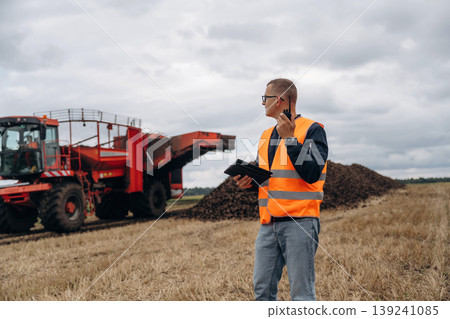 Conversation by walkie talkie. Farmer is working in the agricultural field. Against beet harvester Conversation by walkie talkie. Farmer is working in the agricultural field. Against beet harvester 139241085