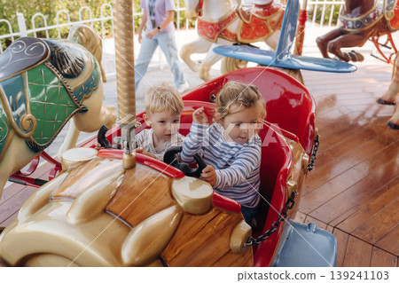 A girl and a boy ride on a carousel, in a car. Happy kids A girl and a boy ride on a carousel, in a car. Happy kids 139241103