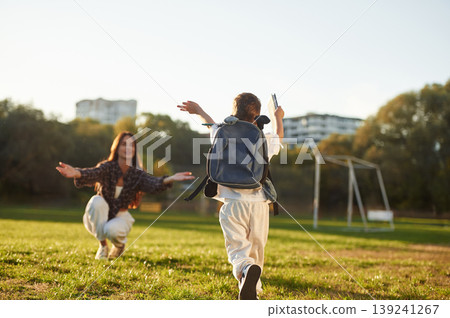 To the hugs, school conception, with backpack. Mother and son together in an open field during daytime To the hugs, school conception, with backpack. Mother and son together in an open field during daytime 139241267