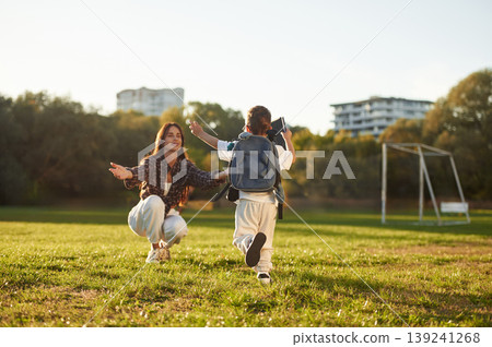 To the hugs, school conception, with backpack. Mother and son together in an open field during daytime To the hugs, school conception, with backpack. Mother and son together in an open field during daytime 139241268