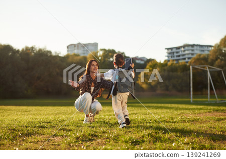 To the hugs, school conception, with backpack. Mother and son together in an open field during daytime To the hugs, school conception, with backpack. Mother and son together in an open field during daytime 139241269