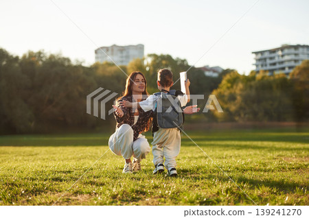 To the hugs, school conception, with backpack. Mother and son together in an open field during daytime To the hugs, school conception, with backpack. Mother and son together in an open field during daytime 139241270