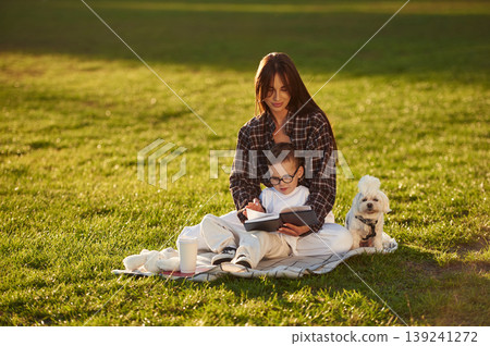 Reading the book, sitting on the blanket. Mother and son together in an open field during daytime 139241272