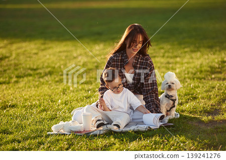 Reading the book, sitting on the blanket. Mother and son together in an open field during daytime Reading the book, sitting on the blanket. Mother and son together in an open field during daytime 139241276