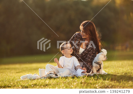 Cute little dog is with them. Mother and son together in an open field during daytime Cute little dog is with them. Mother and son together in an open field during daytime 139241279
