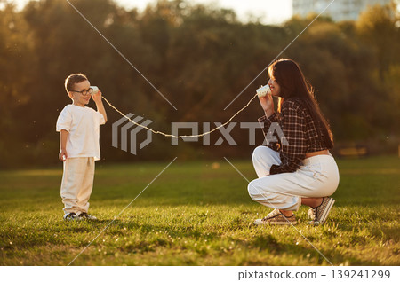 Playing with tin can phone. Mother and son together in an open field during daytime 139241299