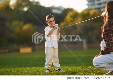 Playing with tin can phone. Mother and son together in an open field during daytime Playing with tin can phone. Mother and son together in an open field during daytime 139241303