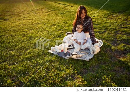 On the picnic blanket. Mother and son together in an open field during daytime On the picnic blanket. Mother and son together in an open field during daytime 139241481