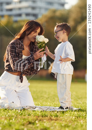 Gives flowers to woman, gift conception. Mother and son together in an open field during daytime Gives flowers to woman, gift conception. Mother and son together in an open field during daytime 139241490