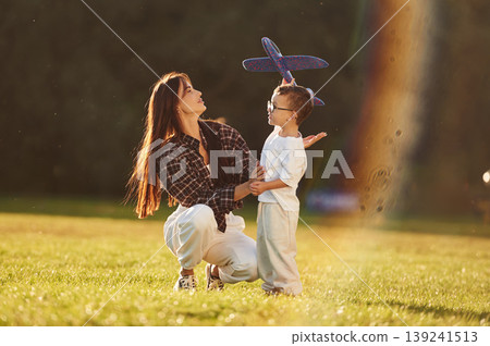 Imagination conception, playing with toy plane. Mother and son together in an open field during daytime Imagination conception, playing with toy plane. Mother and son together in an open field during daytime 139241513