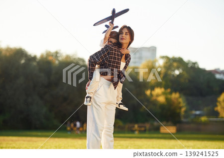 Under sunlight, playing with toy plane. Mother and son together in an open field during daytime Under sunlight, playing with toy plane. Mother and son together in an open field during daytime 139241525