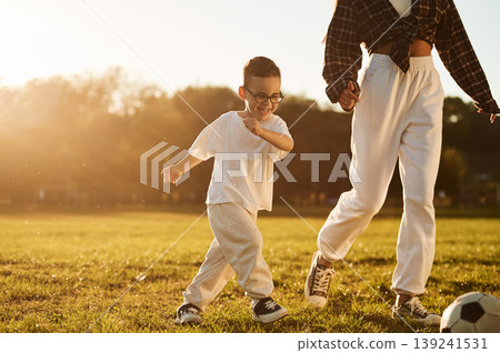 Running, playing soccer. Mother and son together in an open field during daytime Running, playing soccer. Mother and son together in an open field during daytime 139241531
