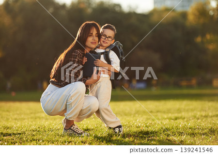 Back to school conception, with backpack. Mother and son together in an open field during daytime Back to school conception, with backpack. Mother and son together in an open field during daytime 139241546